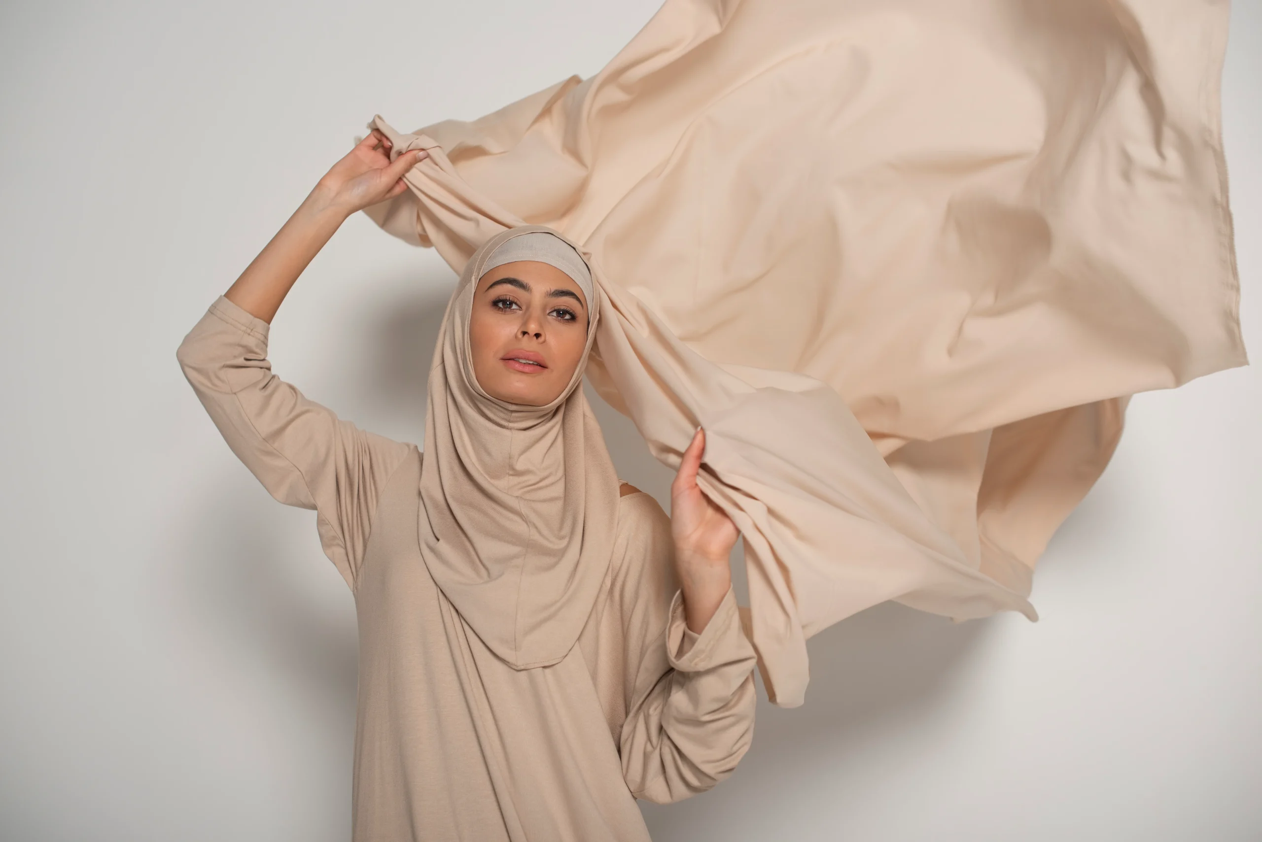 Model wearing soft beige modest abaya with flowing fabric and modern hijab styling